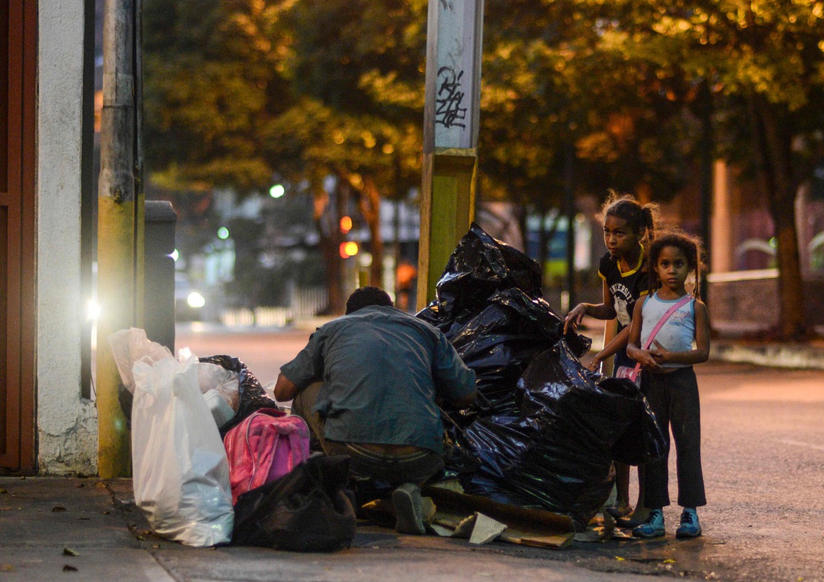A man and two girls scavenge for food in the streets of Caracas on February 21, 2017. Venezuelan President Nicolas Maduro is resisting opposition efforts to hold a vote on removing him from office. The opposition blames him for an economic crisis that has