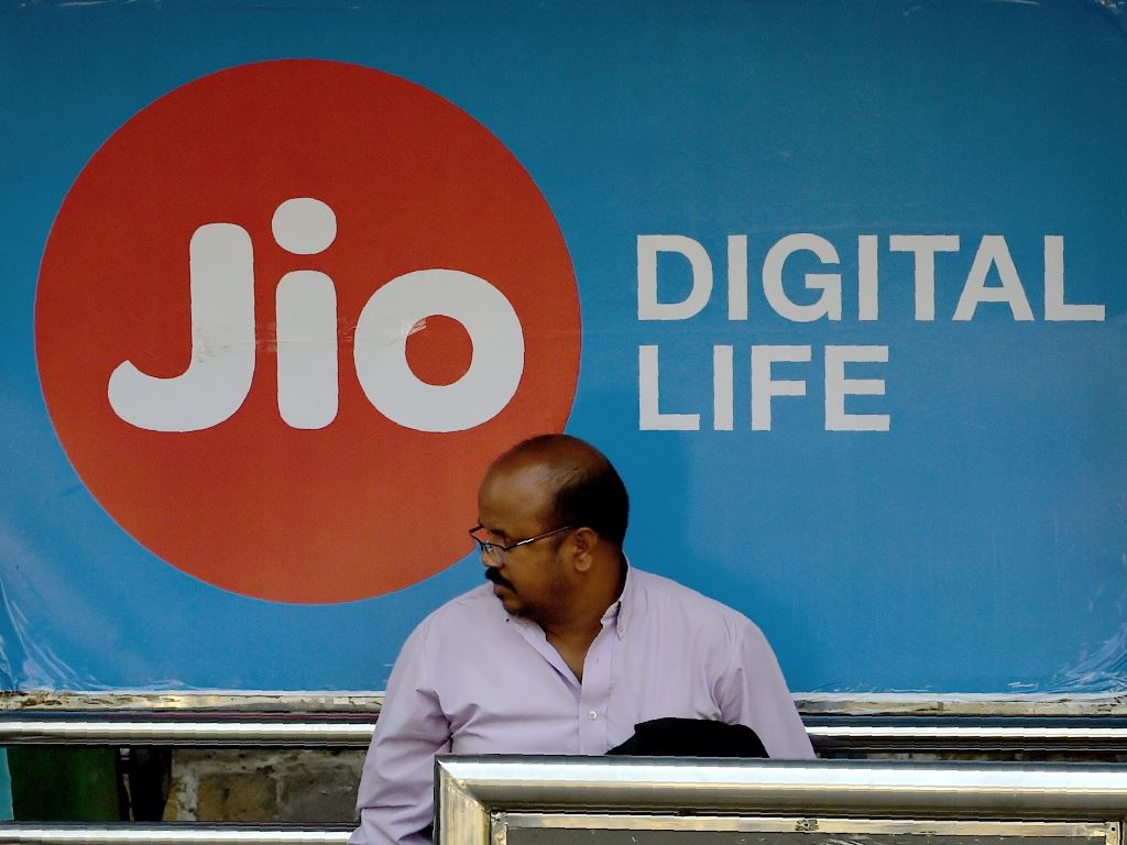 This photo taken on March 7, 2017 shows an Indian man sitting in front of a sign for Indian mobile service provider Jio at a bus stop in Mumbai. AFP / Indranil Mukherjee