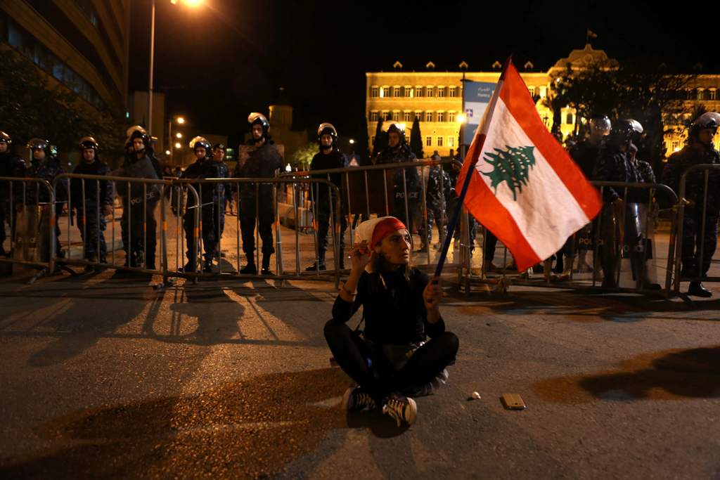 A Lebanese woman holding her national flag sits in the middle of the street as riot police guard the Grand Serail (the prime minister's headquarters) in downtown Beirut on March 16, 2017, during a protest against the Lebanese Parliament's newly approved t