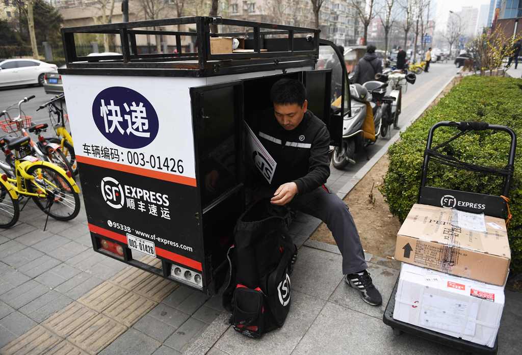 (FILES) This file photo taken on March 17, 2017 shows an SF Express courier delivery rider sorting packages in the back of his tricycle on a sidewalk in Beijing. AFP / Greg Baker