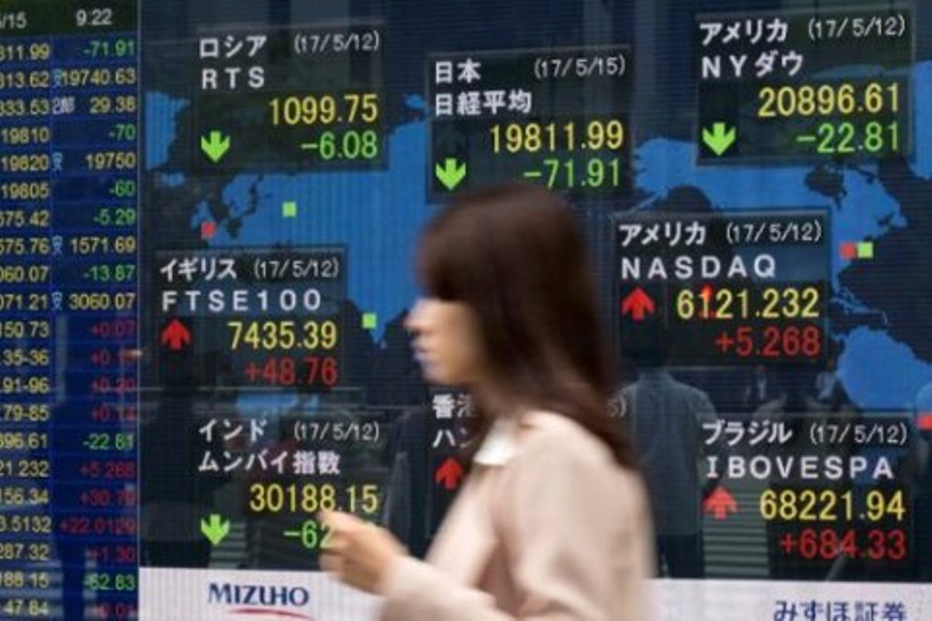 A woman walks past a quotation board displaying numbers of the world stock markets in front of a securities company in Tokyo on May 15, 2017. / AFP.