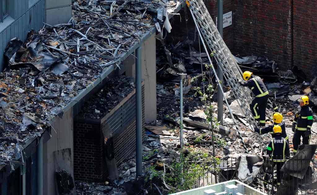 Firefighteres work amongst debris at the base of the charred remnains of the Grenfell Tower block in Kensington, west London, on June 17, following the June 14 fire at the residential building. / AFP.