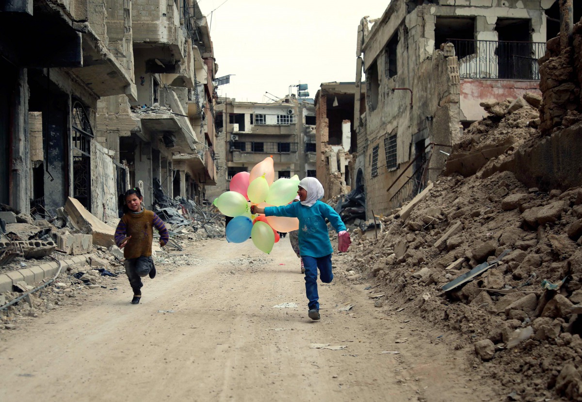 FILE PHOTO: Syrian children run with balloons past heavily damaged buildings in the neighbourhood of Jobar on the eastern outskirts of the Syrian capital Damascus on April 9, 2016 (AFP / Amer Almohibany)