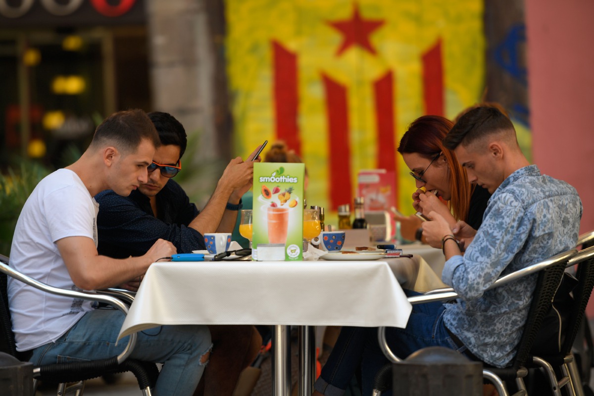 A group of tourists sit in a terrace in front of a graffitti depicting a Catalan pro-independece flag 'Estelada' on September 13, 2017, in Barcelona. AFP / Lluis Gene