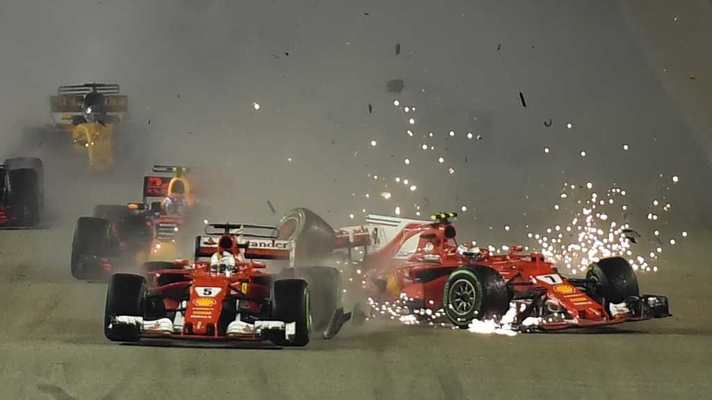 The car of Ferrari's Finnish driver Kimi Raikkonen (R) is seen after a crash as Ferrari's German driver Sebastian Vettel (C) leads during the Formula One Singapore Grand Prix in Singapore on September 17, 2017. / AFP / MANAN VATSYAYANA

