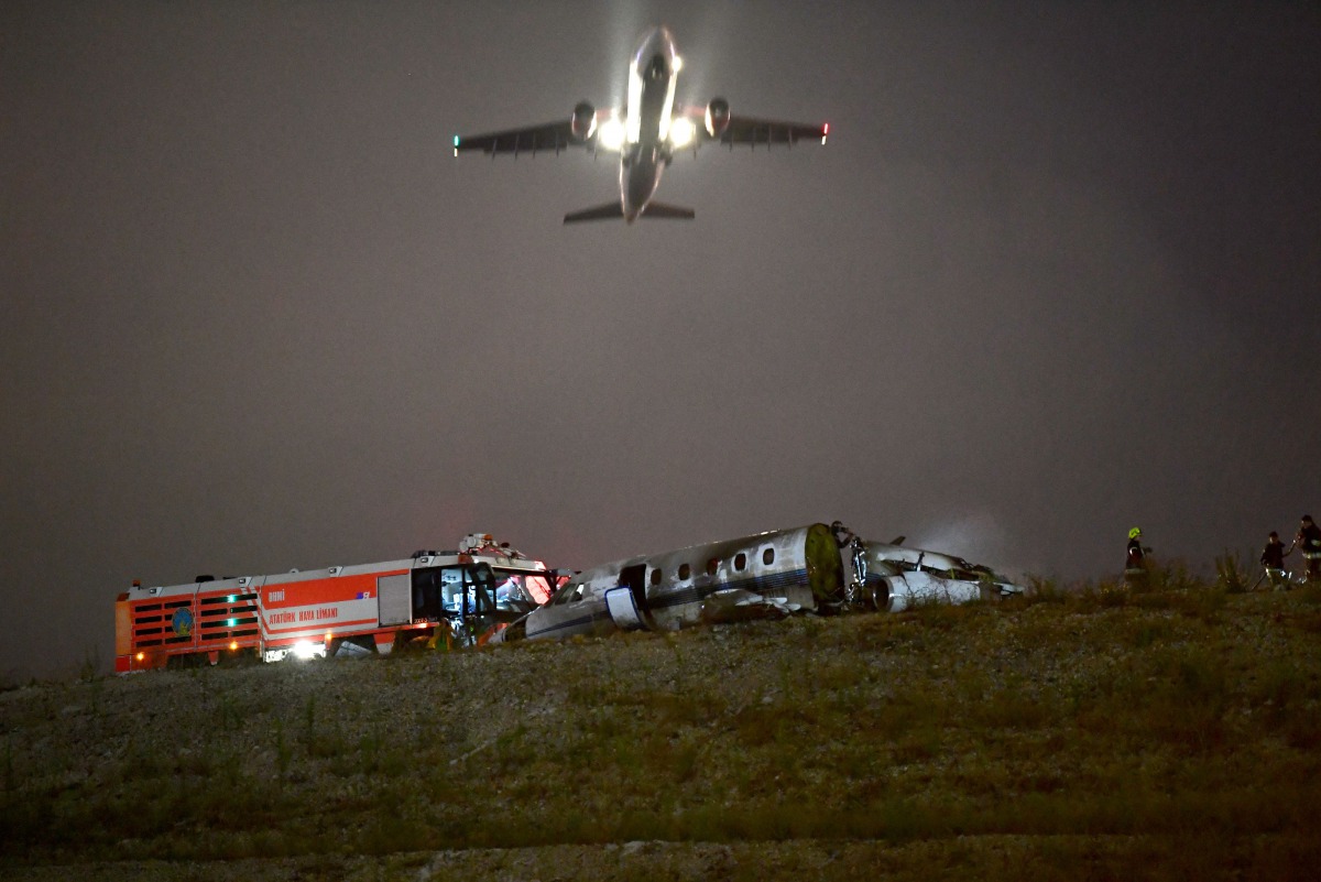 A plane passes as firefighters attempt to extinguish a burning private airplane after crashing at Ataturk Airport on September 21, 2017 in Istanbul.  AFP / Ozan Kose