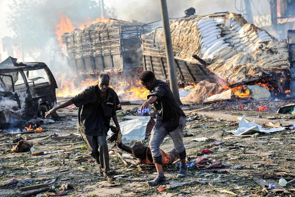Two men carry the body of a victim following the explosion of a truck bomb in the centre of Mogadishu, on October 14, 2017. / AFP.
