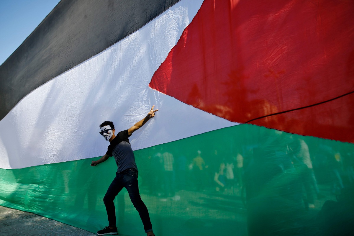 A Palestinian youth poses in front of his national flag during celebrations in Gaza City after rival Palestinian factions Hamas and Fatah reached agreement on October 12, 2017 (AFP / Mohammed Abed) 