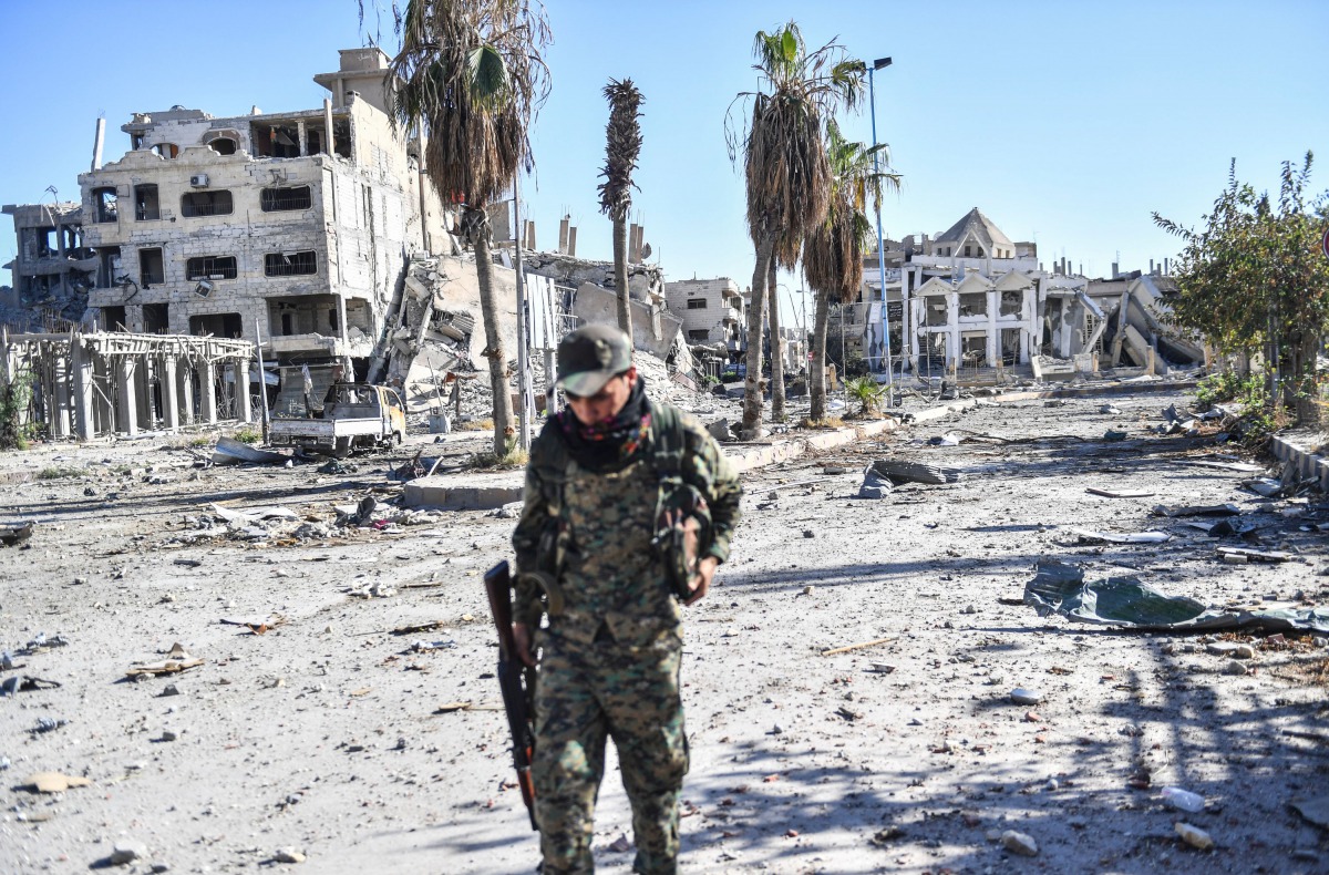 A member of the Syrian Democratic Forces (SDF) walks through a heavily damaged a street leading to an Armenian church in Raqa on October 18, 2017. AFP / Bulent Kilic