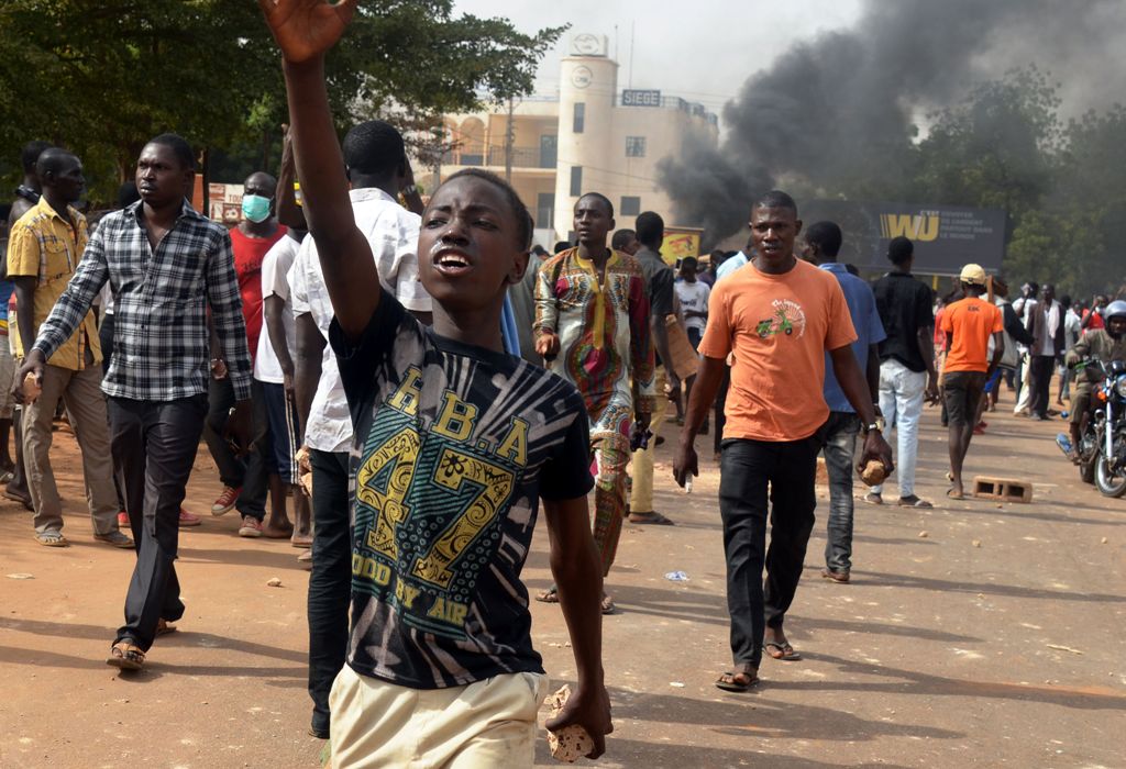 People carry bricks as they walk in front of smoke from a burning tyre during clashes between protesters and police at a demonstration against the 2018 Finance law on October 29, 2017, in Niamey.  AFP / BOUREIMA HAMA
