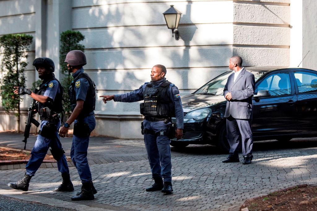 An armed South African Police member gestures as he leaves with colleagues the compound of the controversial business family Gupta while cars belonging to the Hawks, The Directorate for Priority Crime Investigation, are stationed outside, in Johannesburg,
