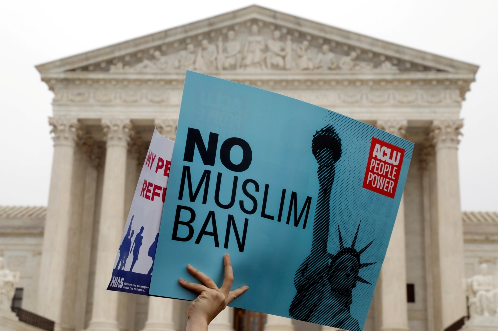 Protesters rally outside the U.S. Supreme Court, while the court justices consider case regarding presidential powers as it weighs the legality of President Donald Trump's latest travel ban targeting people from Muslim-majority countries, in Washington, D
