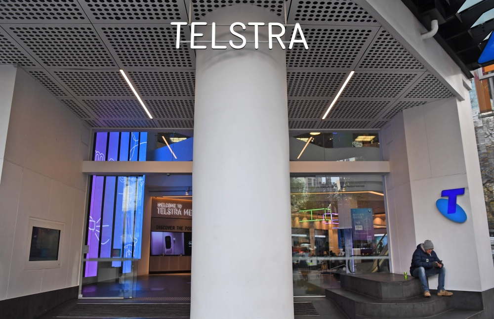 A man (R) sits by the entrance to a Telstra store on Melbourne's central business district on June 20, 2018.  / AFP / William WEST 