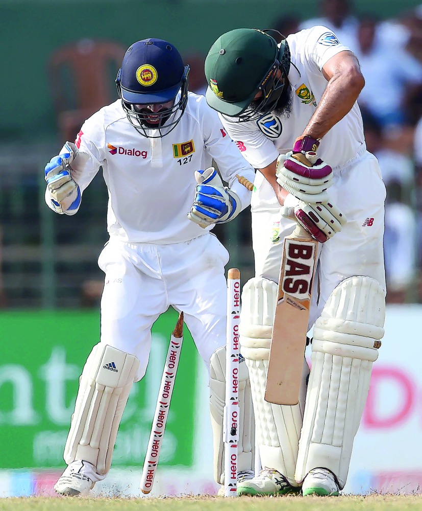 South Africa's Hashim Amla (R) is dismissed by Sri Lankan cricketer Rangana Herath as wicketkeeper Niroshan Dickwella (L) looks on during the third day of their second Test match between Sri Lanka and South Africa at the Sinhalese Sports Club (SSC) intern
