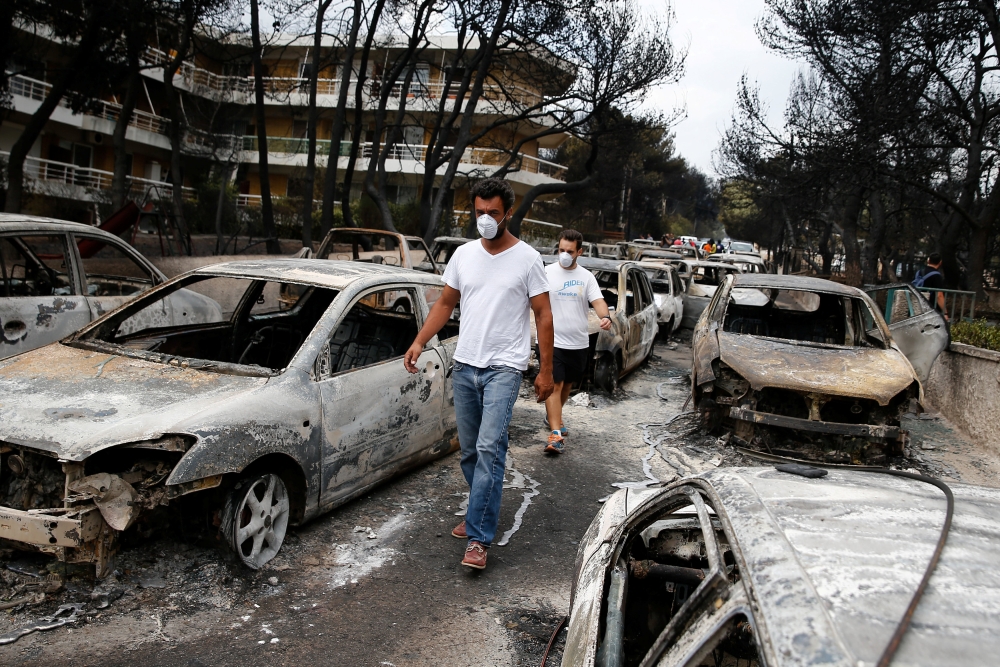 :Locals wearing masks walk among burnt cars following a wildfire at the village of Mati, near Athens, Greece, July 24, 2018. REUTERS/Costas Baltas
