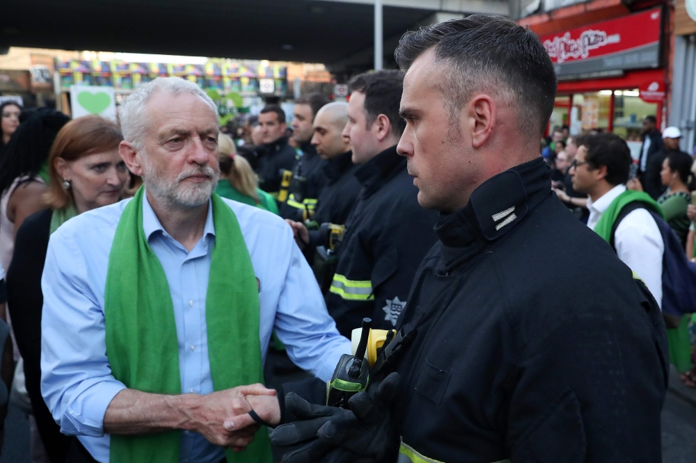 FILE PHOTO: Jeremy Corbyn shakes hands with a fire-fighter lining the street as members of the public take part in a silent march on the first anniversary of the Grenfell fire on June 14, 2018. (AFP / Daniel Leal-Olivas) 