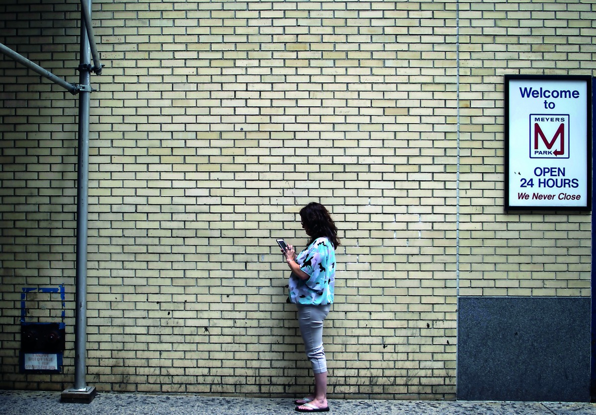 A woman stands to the side of a busy sidewalk to look at her mobile phone in New York on August 21, 2018. AFP / Andrew Caballero-Reynolds