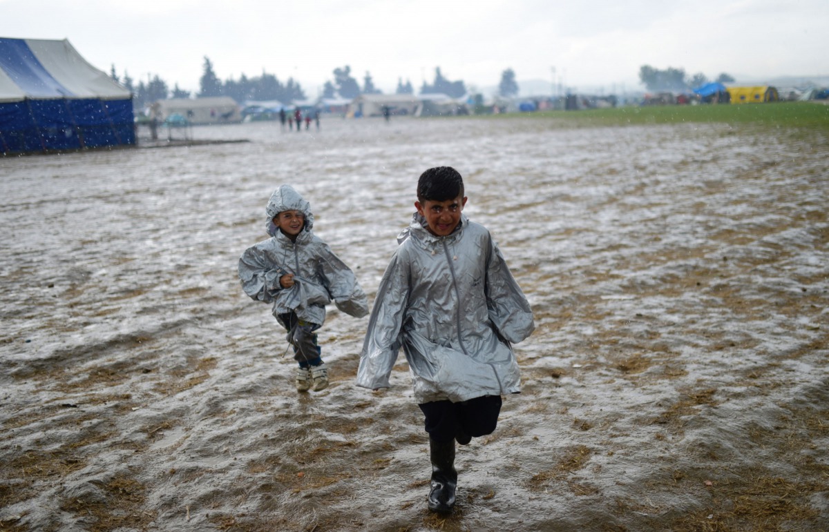 Children refugees run under the rain to get a place on the food line at their makeshift camp in the northern border village of Idomeni, Greece, on April 9, 2016. AFP/Bulent Kilic