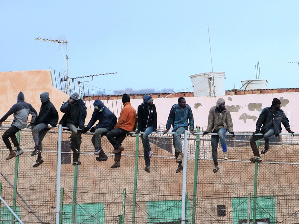 FILE PHOTO: Migrants sit atop a border fence separating Morocco from the north African Spanish enclave of Melilla in the first attempt to jump since the camp on Mount Gurugu burned down.   AFP / ANGELA RIOS

