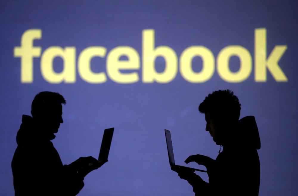 Silhouettes of laptop users are seen next to a screen projection of Facebook logo in this picture illustration (Reuters/Dado Ruvic)