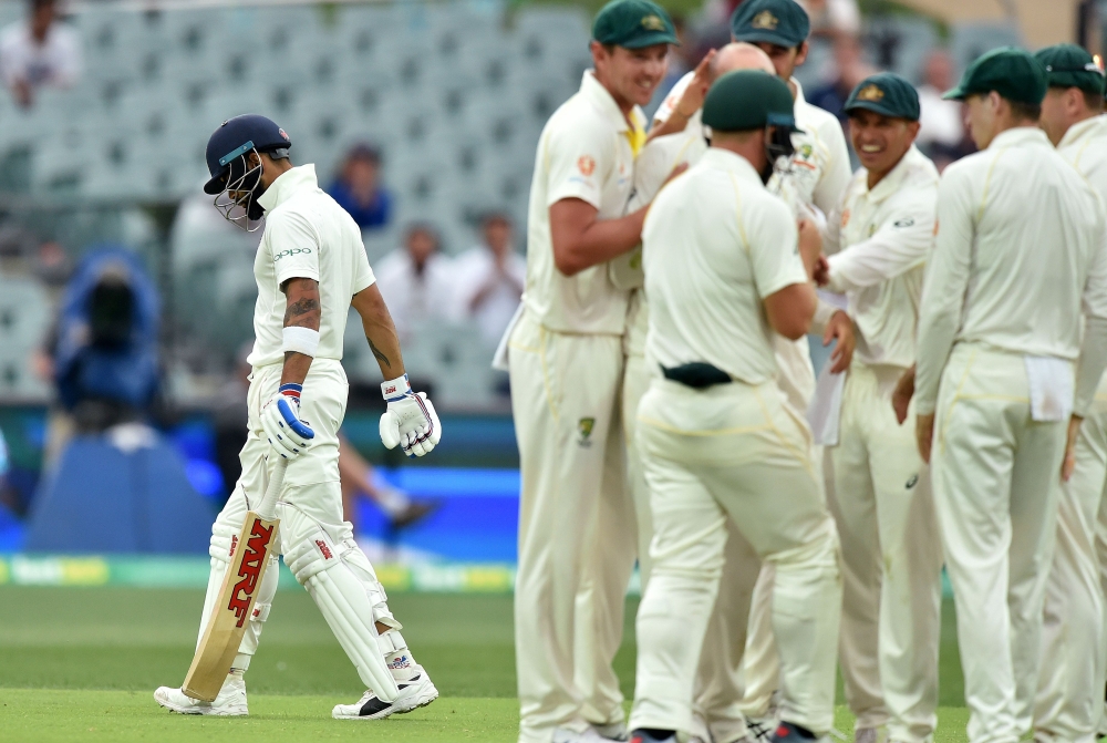 India's captain Virat Kohli (L) walks as Australia's team celebrates his wicket during day three of the first Test cricket match at the Adelaide Oval on December 8, 2018. (AFP / Peter PARKS)