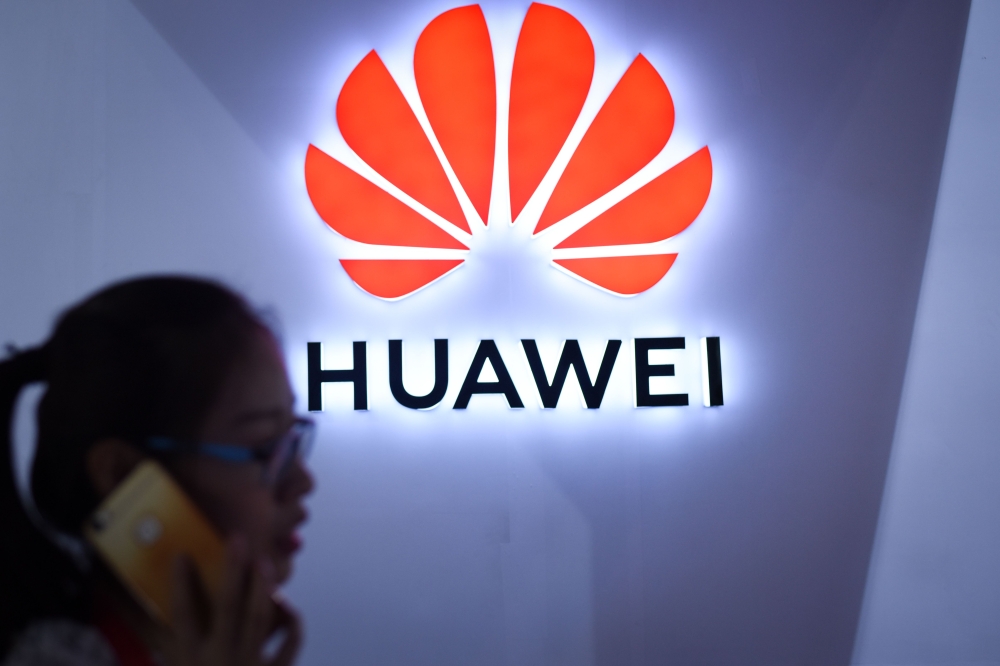 FILE PHOTO: In this file photo taken on July 08, 2018 (FILES) In this file photo taken on July 8, 2018 a woman uses her mobile phone in front of a Huawei logo at Beijing International Consumer Electronics Expo in Beijing.  AFP / WANG ZHAO