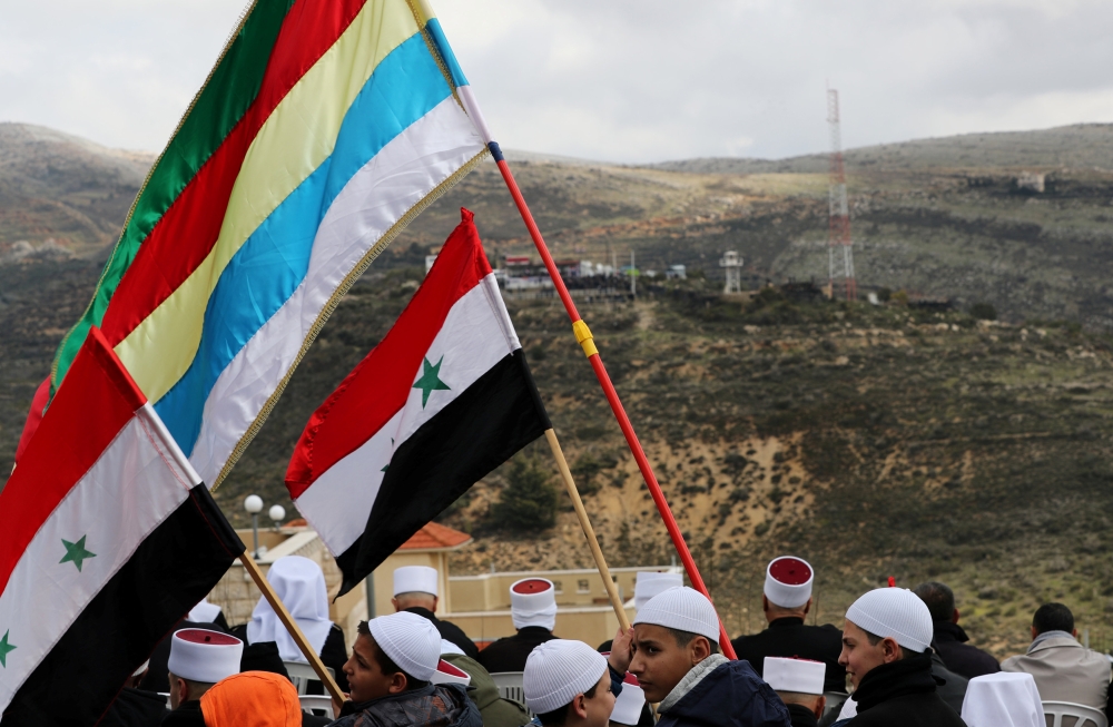 Druze community members holds Syrian and Druze flags as they sit facing Syria, during a rally marking the anniversary of Israel's annexation of the Golan Heights in the Druze village of Majdal Shams in Golan Heights February 14, 2019. Reuters/Ammar Awad 