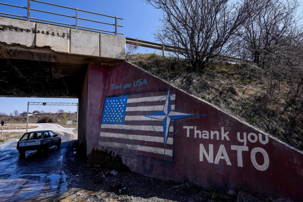 A car drives past a graffiti reading 'Thank You Nato' and featuring the US flag near the village of Stagovo on March 24, 2019. AFP / Armend NIMANI