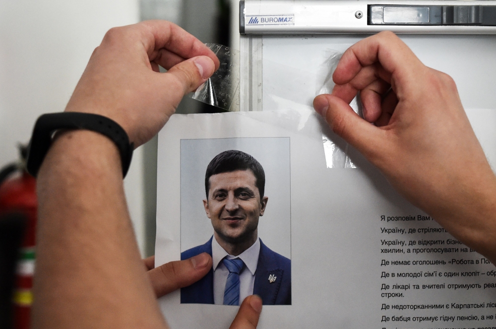 A member of a local electoral commission hangs an information placard bearing a portait of Ukrainian comedian and presidential candidate Volodymyr Zelensky as he prepares a polling station for the upcoming presidential election in Kiev, on April 20, 2019 