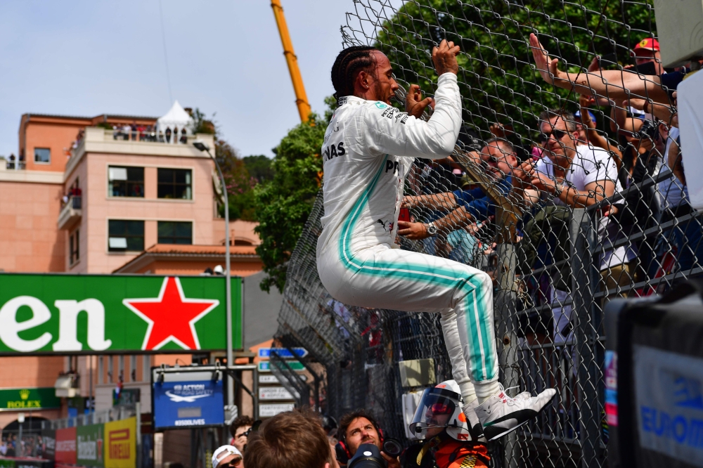 First placed Mercedes' British driver Lewis Hamilton (L) almost bends over after jumping at a fence to greet fans as he celebrates winning the pole position after the qualifying session at the Monaco street circuit on May 25, 2019 in Monaco, ahead of the 