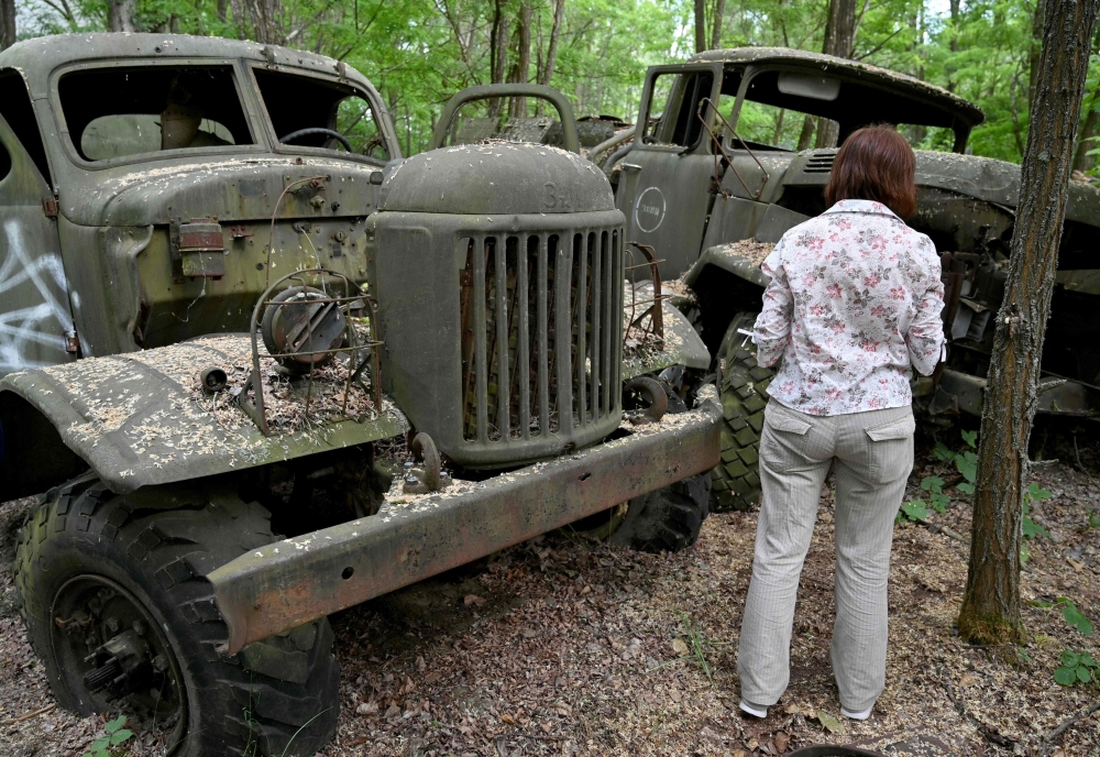 A woman looks at wreckage of trucks in the ghost city of Pripyat during a tour in the Chernobyl exclusion zone on June 7, 2019.  AFP / Genya Savilov 