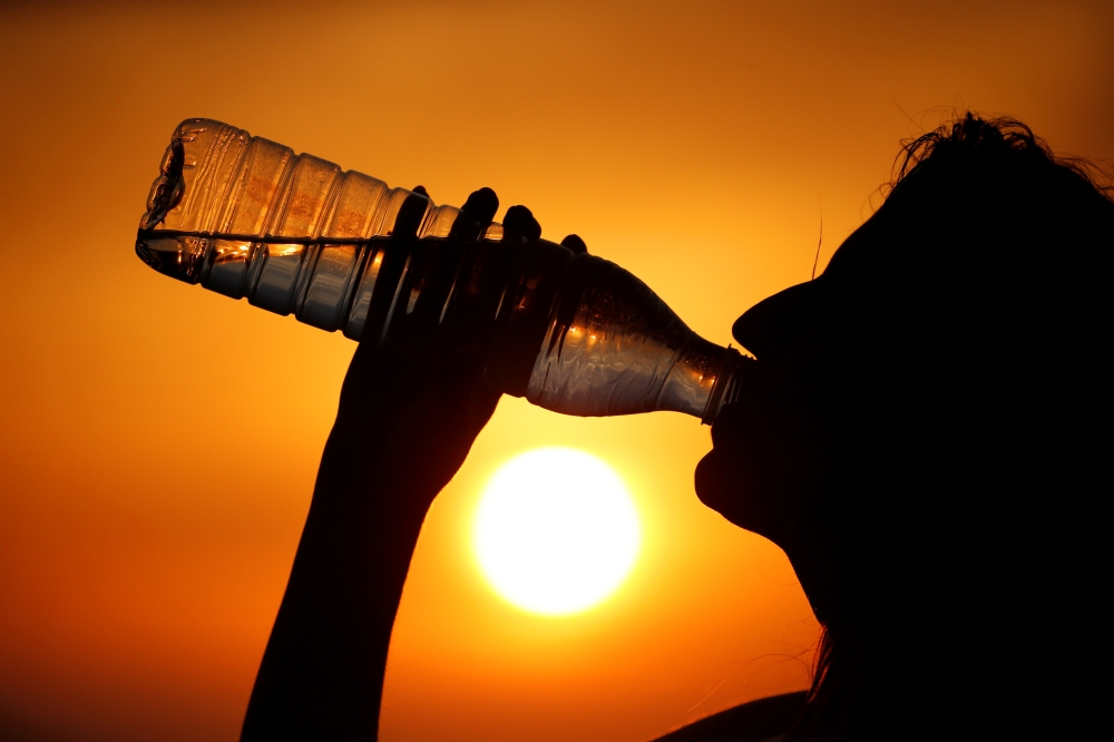 A woman drinks water during sunset, as a heatwave hits France, in Cagnicourt near Cambrai, France, June 25, 2019. Reuters/Pascal Rossignol