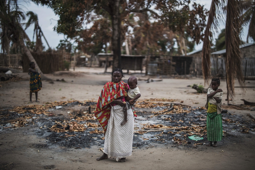 A woman holds her younger child while standing in a burned out area in the recently attacked village of Aldeia da Paz outside Macomia, on August 24, 2019.  AFP / Marco Longari 