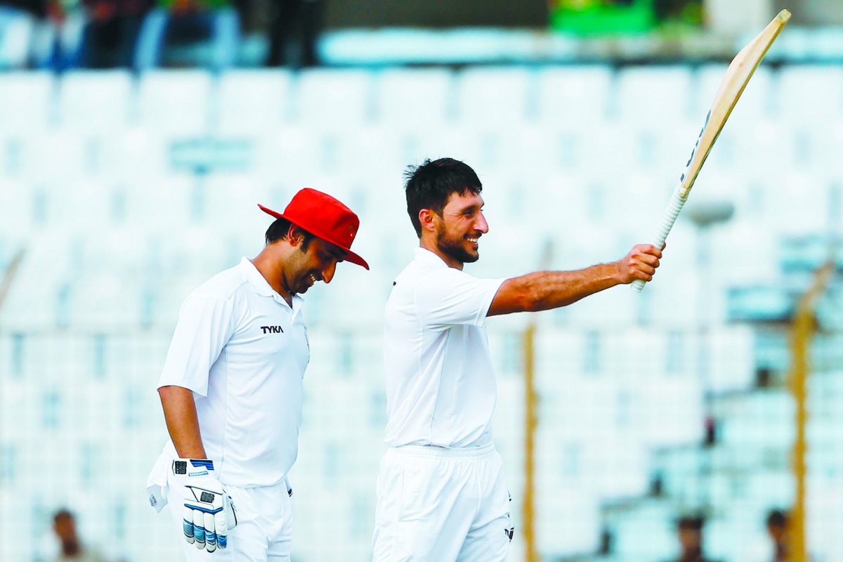 Afghanistan's cricketer Rahman Shah (R) raises his bat to celebrate scoring a century (100 runs) during the first day of the one-off cricket Test match between Bangladesh and Afghanistan at the Zohur Ahmed Chowdhury Stadium in Chittagong on September 5, 2