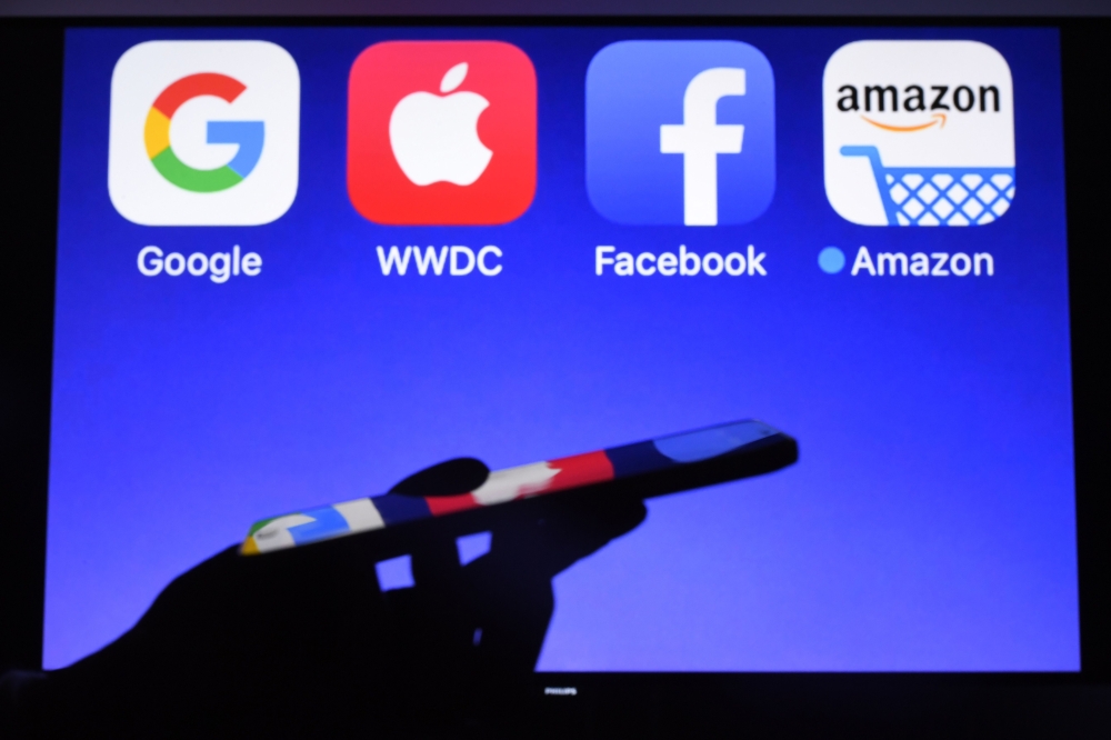 A smartphone being operated in front of Google, Apple, Facebook and Amazon as background in Hédé-Bazouges, western France on September 28, 2017. AFP / Damien Meyer