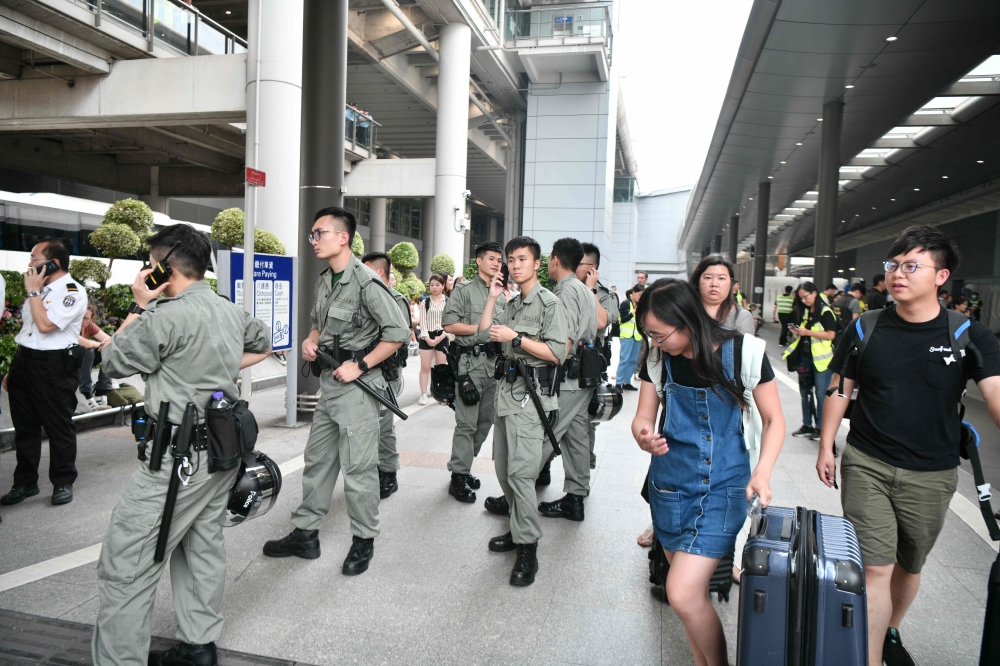 Passengers roll their luggage past police outside Chek Lap Kok International Airport in Hong Kong on September 7, 2019. AFP / Anthony Wallace 