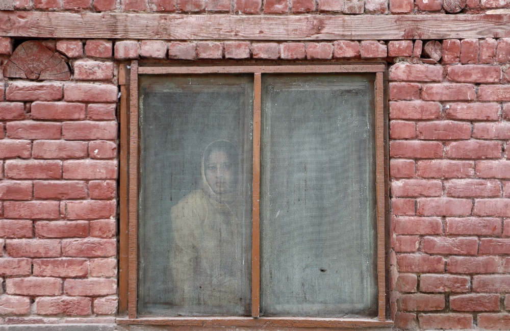 A Kashmiri woman looks out from a window of a house as protesters pass by, after Friday prayers during restrictions, following scrapping of the special constitutional status for Kashmir by the Indian government, in Srinagar, September 20, 2019. REUTERS/Fr