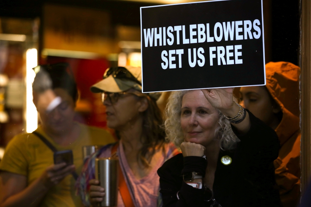 A woman holds a sign about whistleblowers in a cafe near U.S. President Donald Trump’s motorcade as he attends a campaign fundraiser nearby in New York, U.S. September 26, 2019. (REUTERS/Jonathan Ernst)