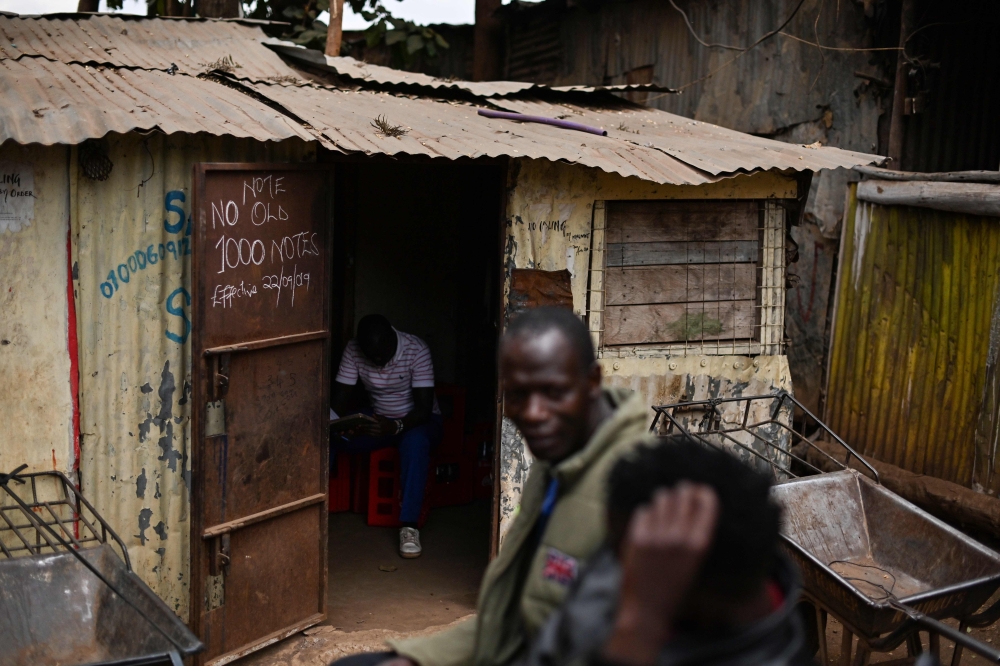 Residents of Kibera slum in Kenya's capital Nairobi sit outside a makeshift soda depot on September 26, 2019 with a notification inscribed on the door to clients that payments in the old tender notes are no longer accepted. AFP / Tony Karumba 
