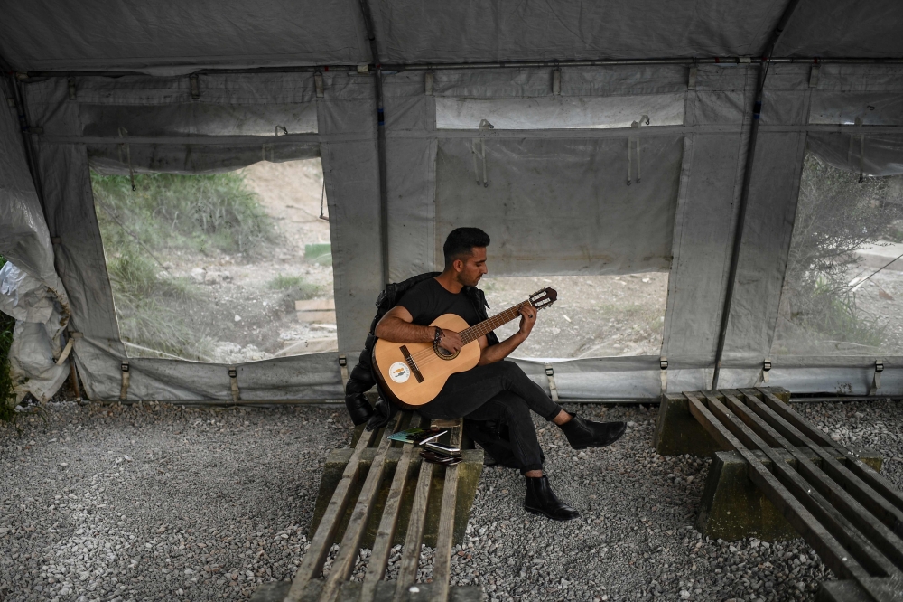 File photo: A man plays the guitar at an unofficial camp outside the refugee camp of Moria on the Greek island of Lesbos on March 19. 2019. AFP / Aris Messinis