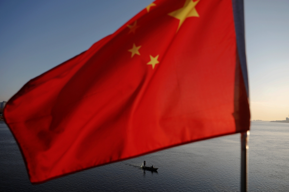 N Korean fishermen are seen as a Chinese flag flutters from the Broken Bridge as the sun sets over Yalu River between N Korean town of Sinuiju Dandong in Liaoning Province, China, Nov 19, 2017. Reuters / Damir Sagolj