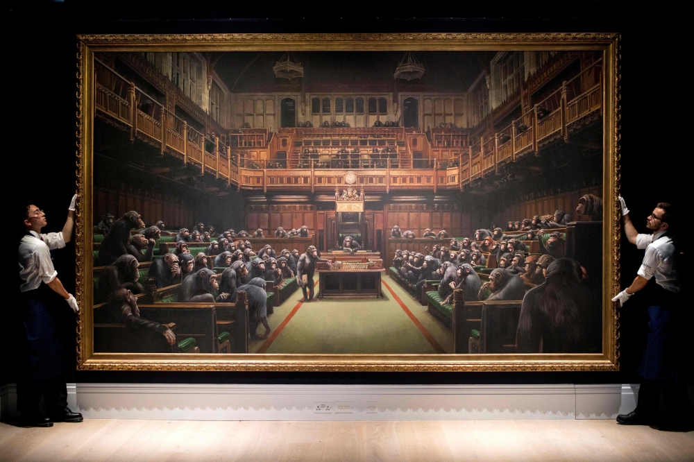 (FILES) In this file photo taken on September 27, 2019 Gallery assistants pose with an artwork entitled 'Devolved Parliament' by British artist Banksy, during a press view in London. AFP / Tolga Akmen