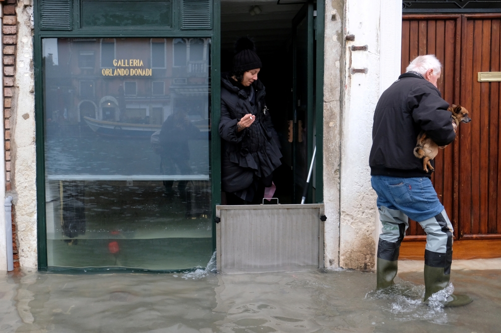 A man with his dog walks past an art gallery during exceptionally high water levels in Venice, Italy November 13, 2019. REUTERS/Manuel Silvestri