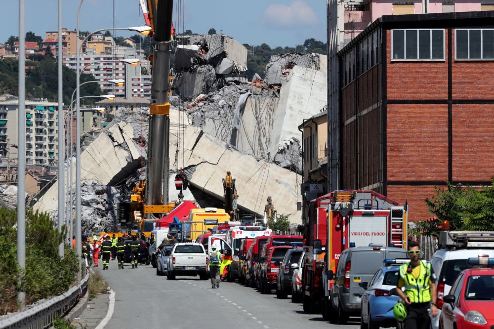 Firefighters and rescue workers stand at the site of a collapsed Morandi Bridge in the port city of Genoa, Italy August 15, 2018. Reuters/Stefano Rellandini
