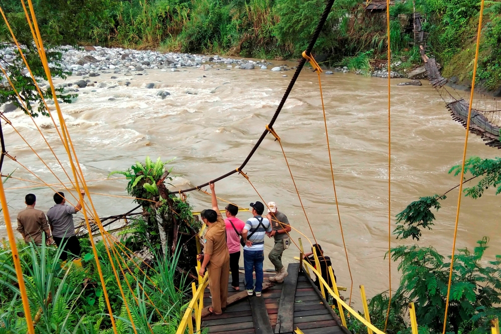 Locals and rescue workers stand on the remains of a footbridge that collapsed following heavy rains as they search for the missing in Kaur regency, Bengkulu province, Indonesia, January 20, 2020 in this photo taken by Antara Foto. Picture taken January 20