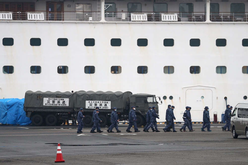 Japan Self-Defense Forces members walk past a military vehicle attached to a gate of the Diamond Princess cruise ship, which has around 3,600 people quarantined onboard due to fears of the new COVID-19 coronavirus, at the Daikoku Pier Cruise Terminal in Y