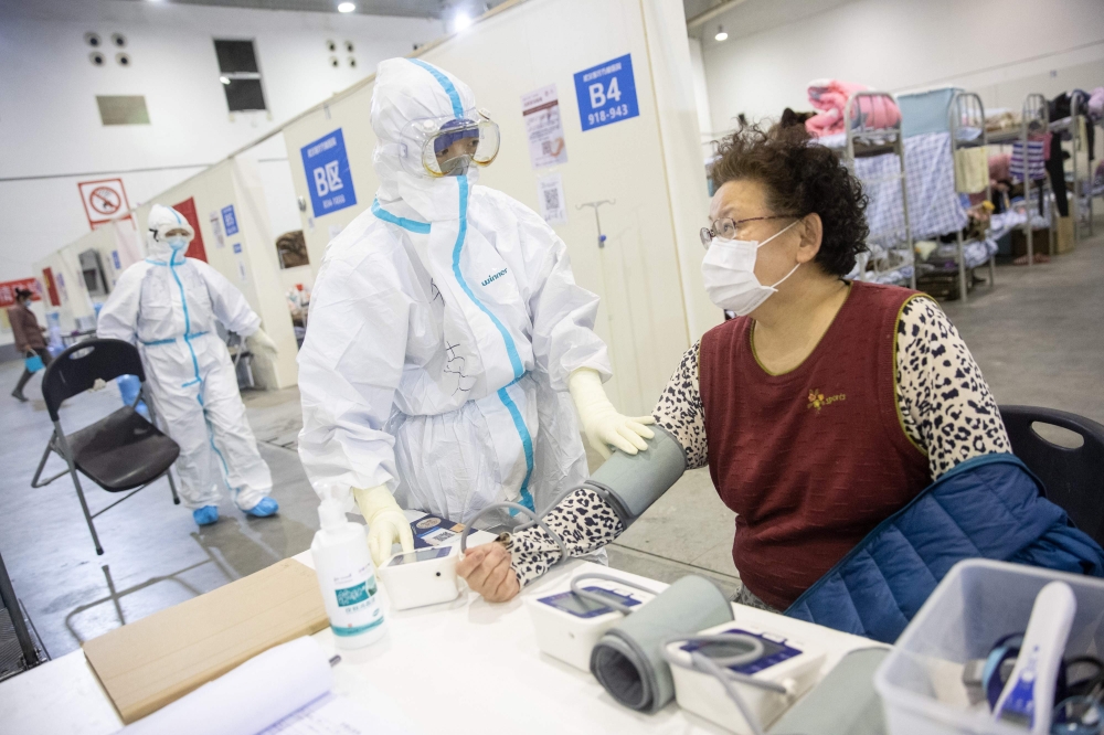 This photo taken on February 17, 2020 shows a member of the medical staff (C) taking the blood pressure of a woman who has displayed mild symptoms of the COVID-19 coronavirus at an exhibition centre converted into a hospital in Wuhan in China's central Hu