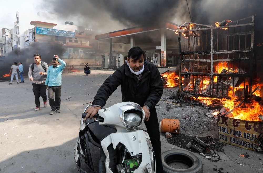 A man pushes his damaged scooter past a burning petrol pump during a clash between people supporting a new citizenship law and those opposing it, in New Delhi India, February 24, 2020. REUTERS/Danish Siddiqui