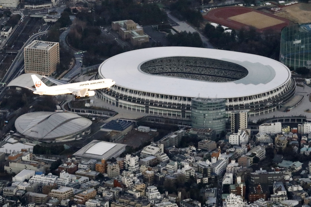An airplane flying near National Stadium in a test of the new flight paths for international passenger aircraft bound for Haneda Airport, in Tokyo, Japan, February 2, 2020. Credit: Kyodo via Reuters