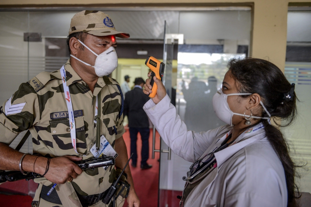 A health worker (R) checks the temperature of a Central Industrial Security Force personnel (L) amid concerns of the spread of the COVID-19 coronavirus, at the entrance of the Wings India 2020 international exhibition at Begumpet Airport in Hyderabad on M